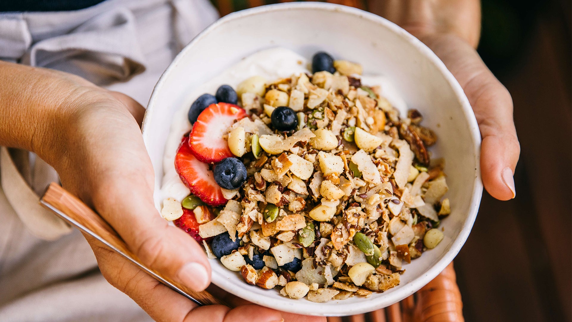 Bowl of Keto Premium Paleo Granola with strawberries, blueberries and yoghurt being held by woman