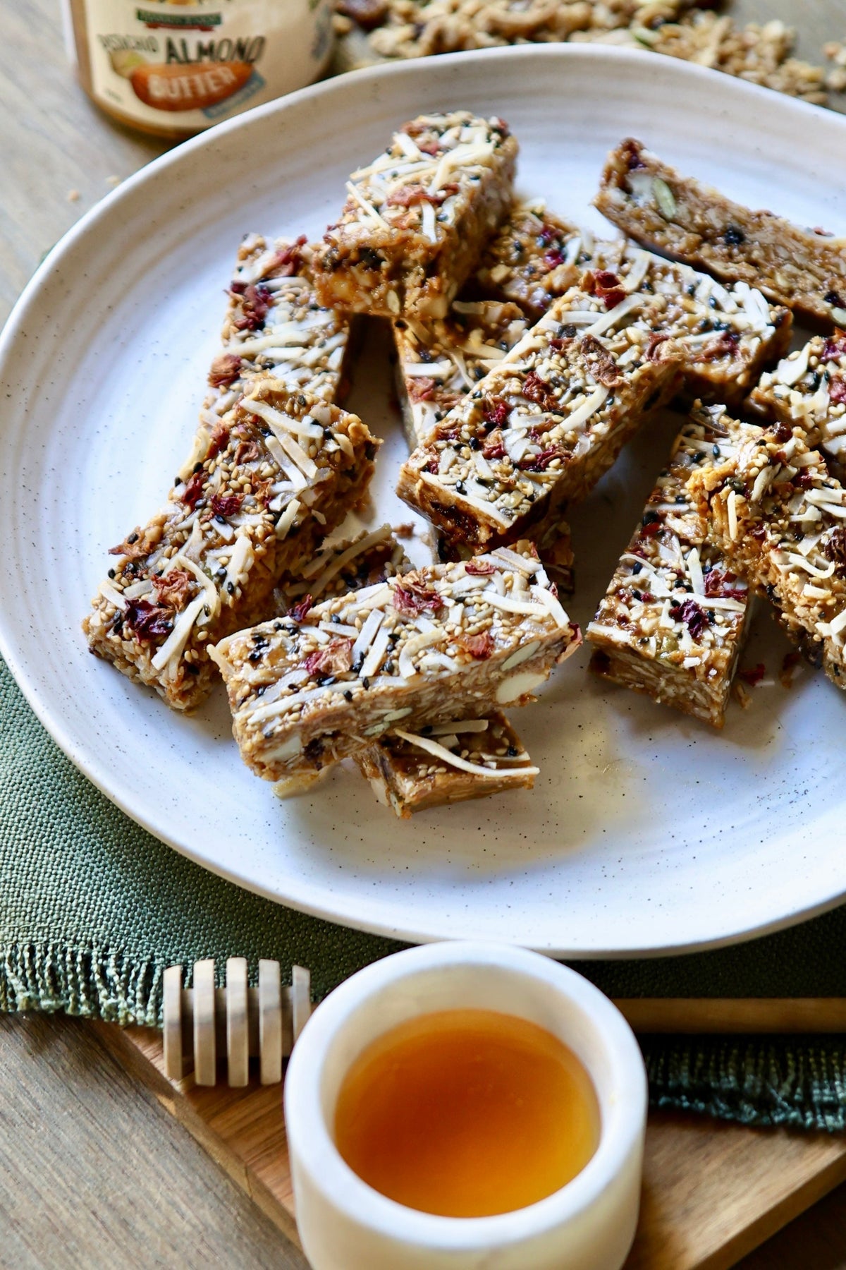 Macadamia and cranberry muesli bars on a white plate with a bowl of honey.