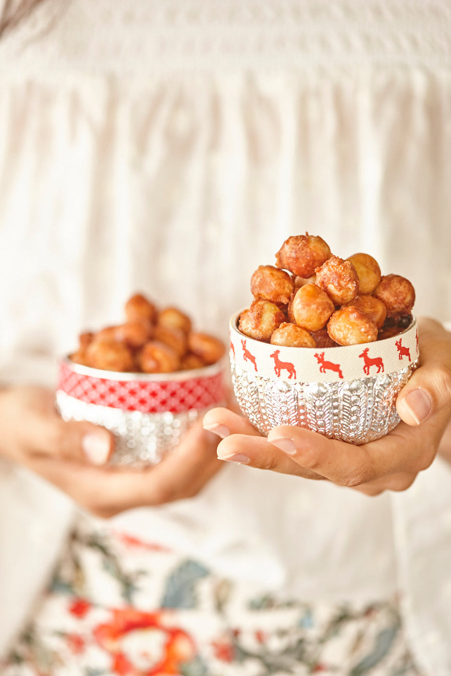 Hands holding two decorative silver bowls filled with candied macadamias