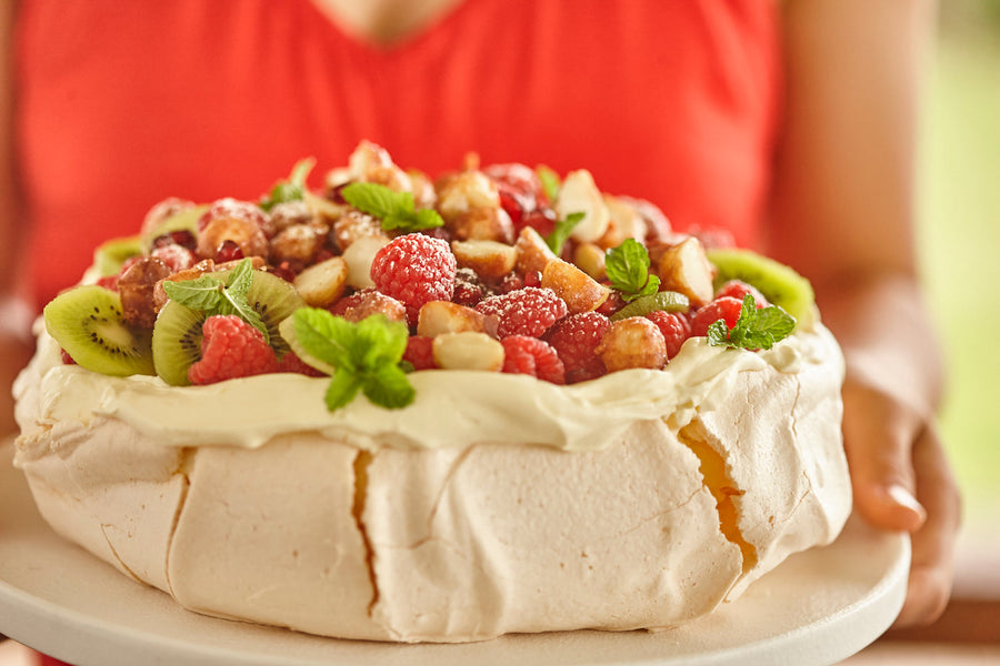 Pavlova topped with whipped cream, seasonal berries, kiwi, and candied macadamias