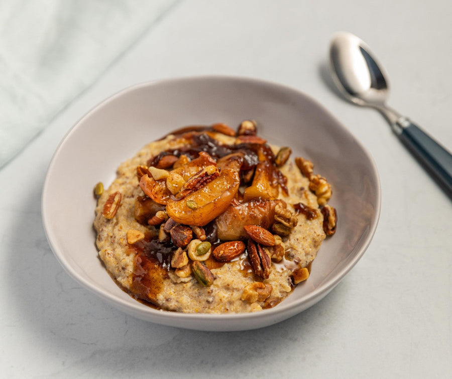 Bowl of creamy porridge topped with roasted maple apples, nuts, and seeds.