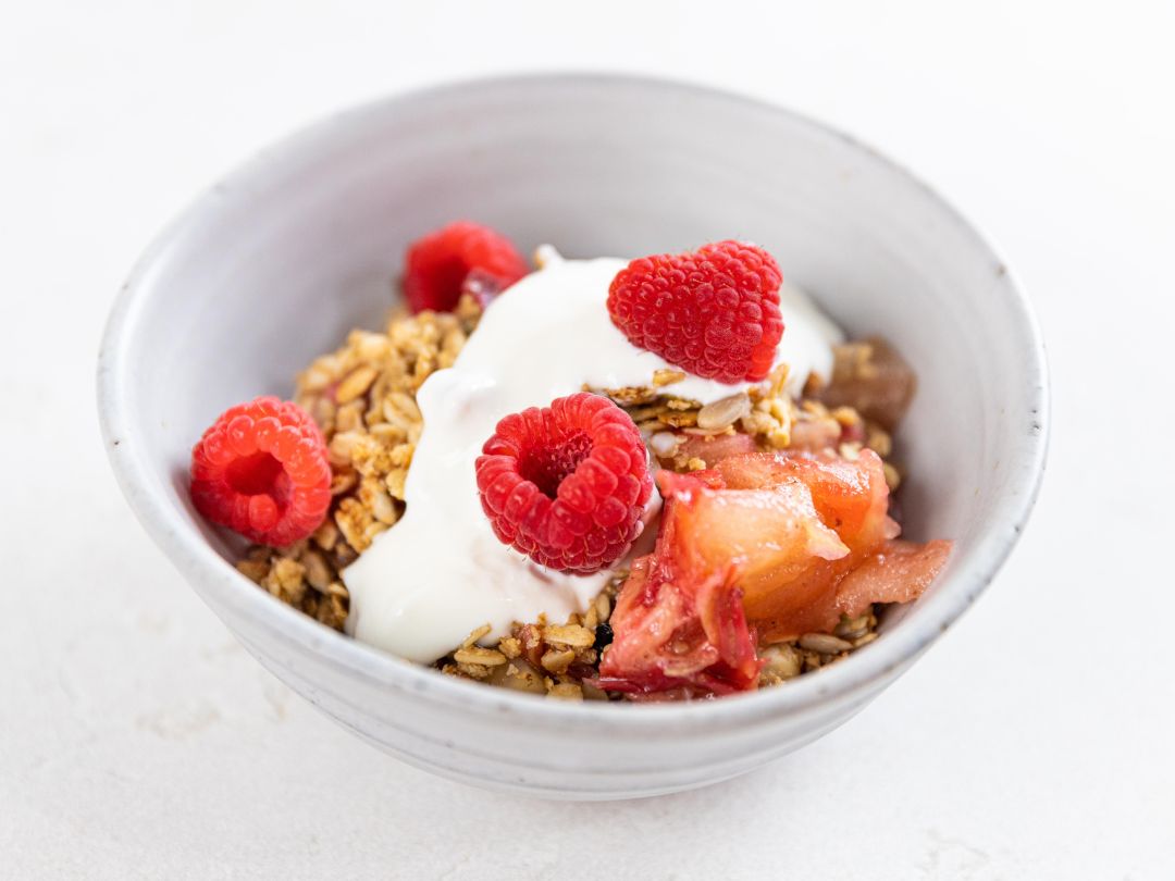 Apple rhubarb muesli crumble bowl topped with yogurt and fresh raspberries