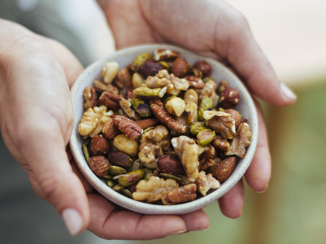Hands holding a small bowl of premium mixed nuts and seeds