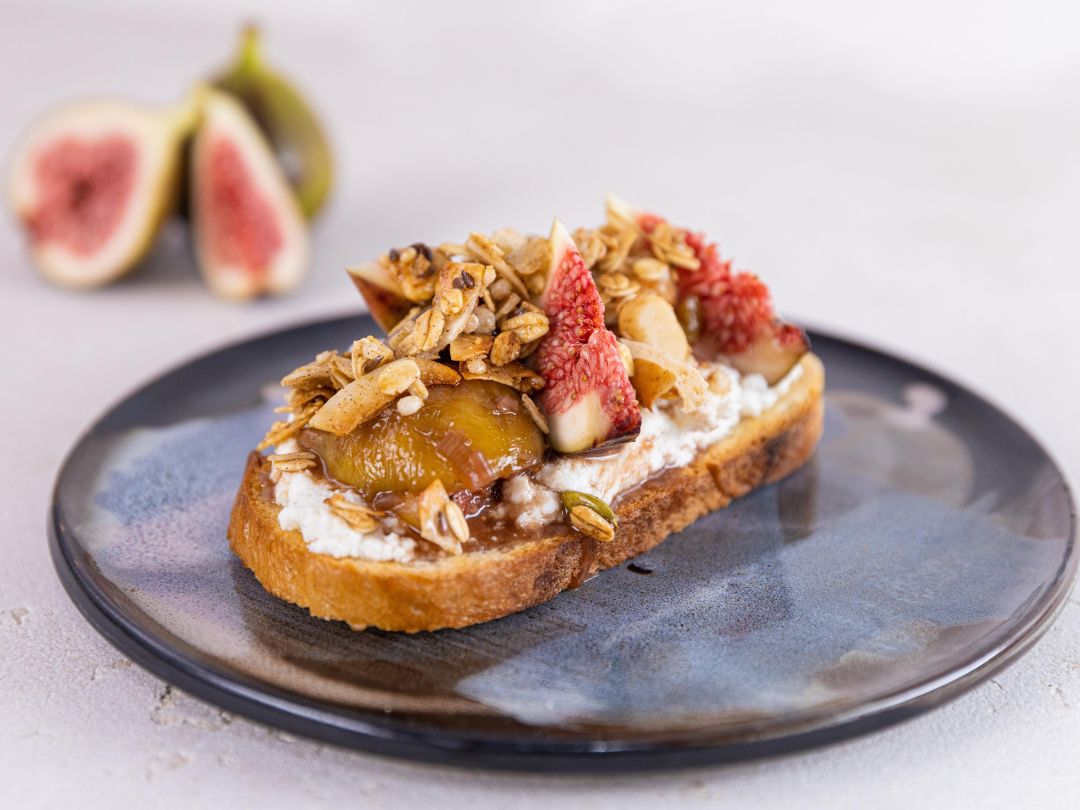Fig toast topped with creamy ricotta, caramelized figs, and nutty macadamia granola on a plate.