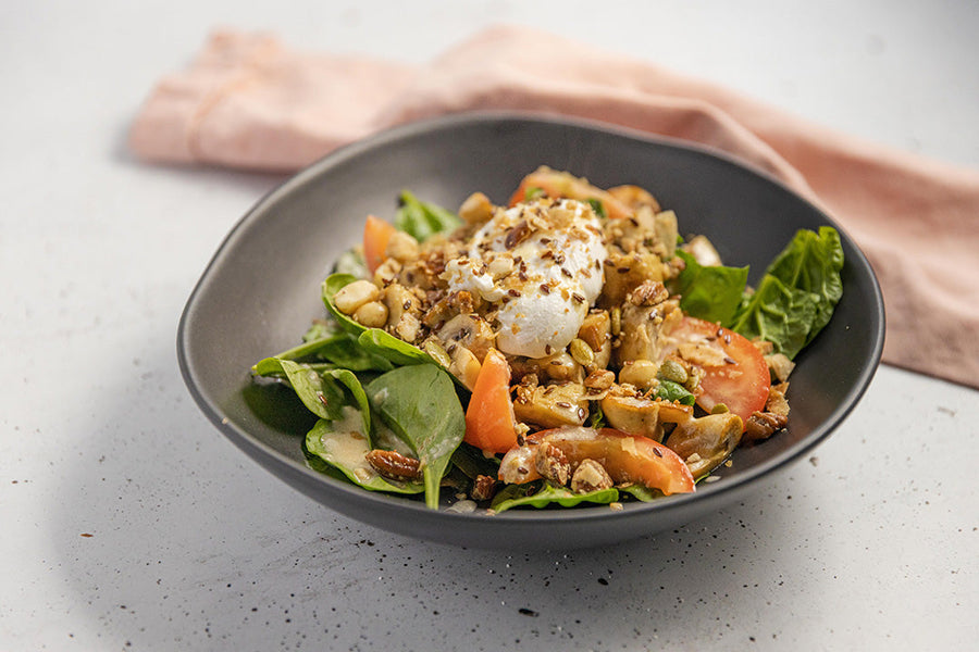Mushroom breaky bowl with poached egg, fresh spinach, cherry tomatoes, and granola in a dark bowl.