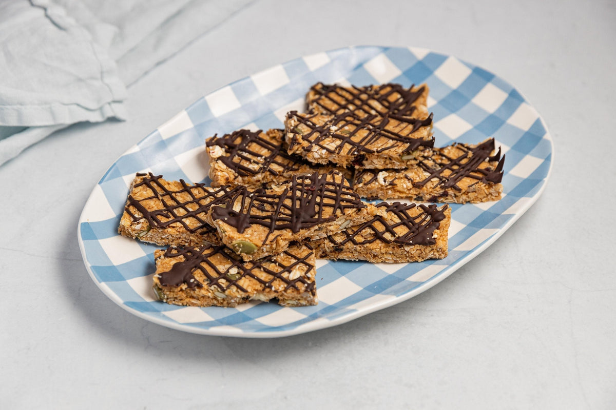 Homemade muesli bars drizzled with chocolate on a blue and white checkered platter