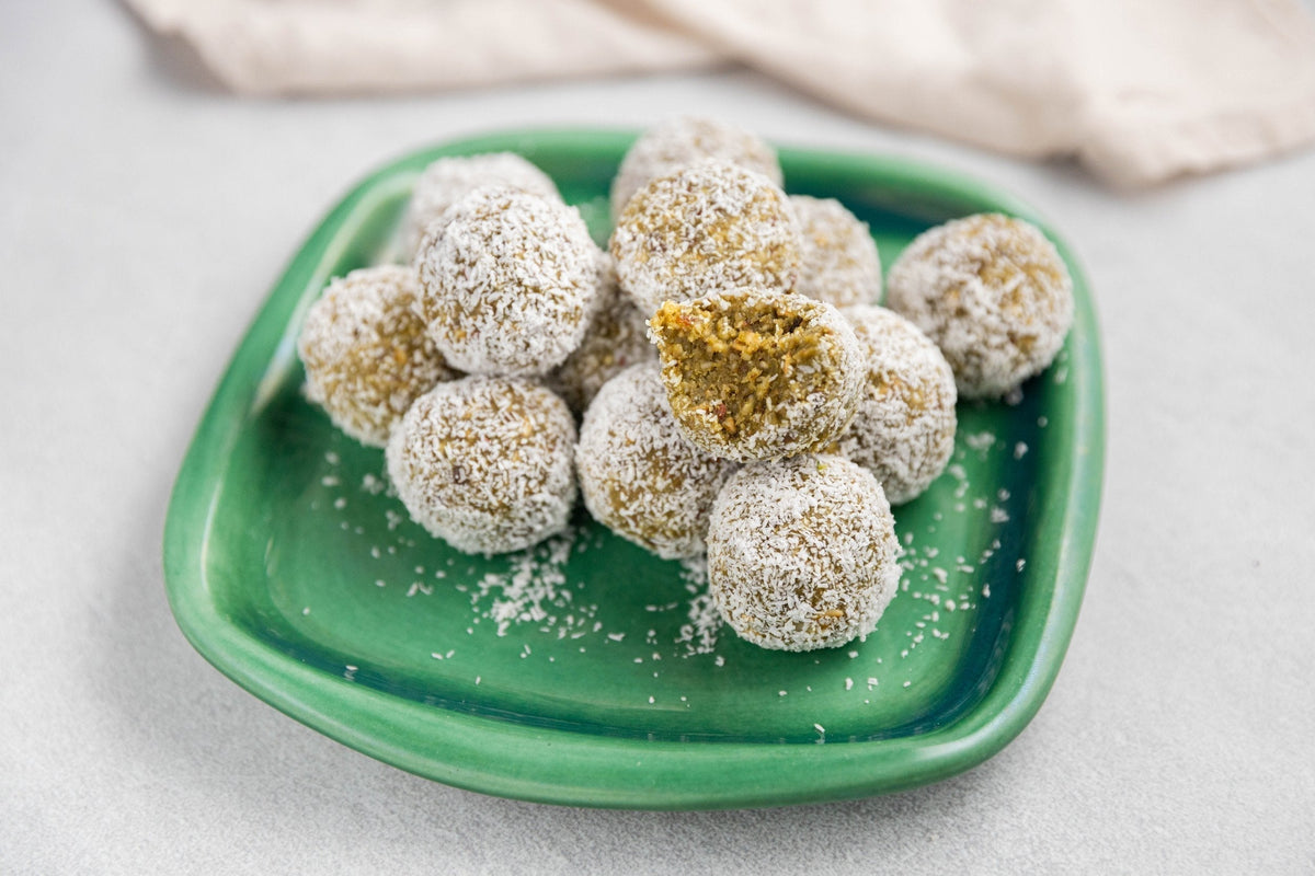 Matcha muesli balls coated in shredded coconut on a green ceramic plate
