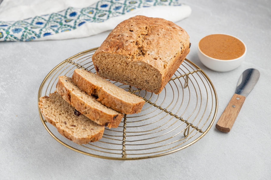 Sliced muesli bread on a wire cooling rack with a side of nut butter.