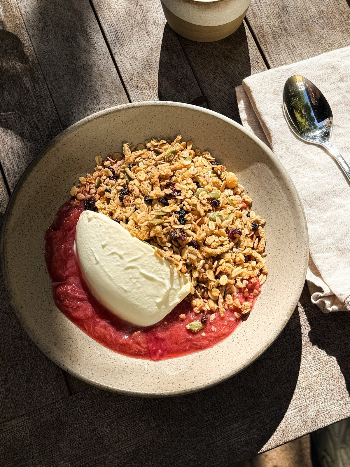 Macadamia cranberry muesli with a dollop of yoghurt and stewed rhubarb in a ceramic bowl
