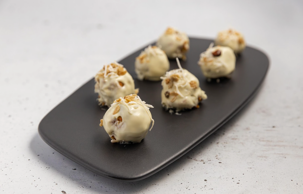 White chocolate coated Carrot Cake Balls with nut toppings on a matte black platter.