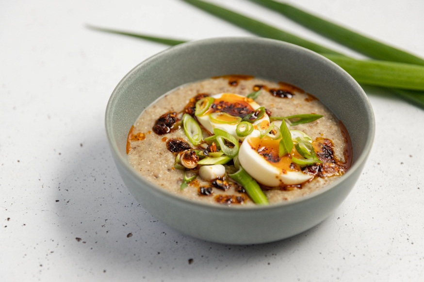 Savoury porridge topped with a soft-boiled egg, sliced spring onions, and chili oil in a bowl.