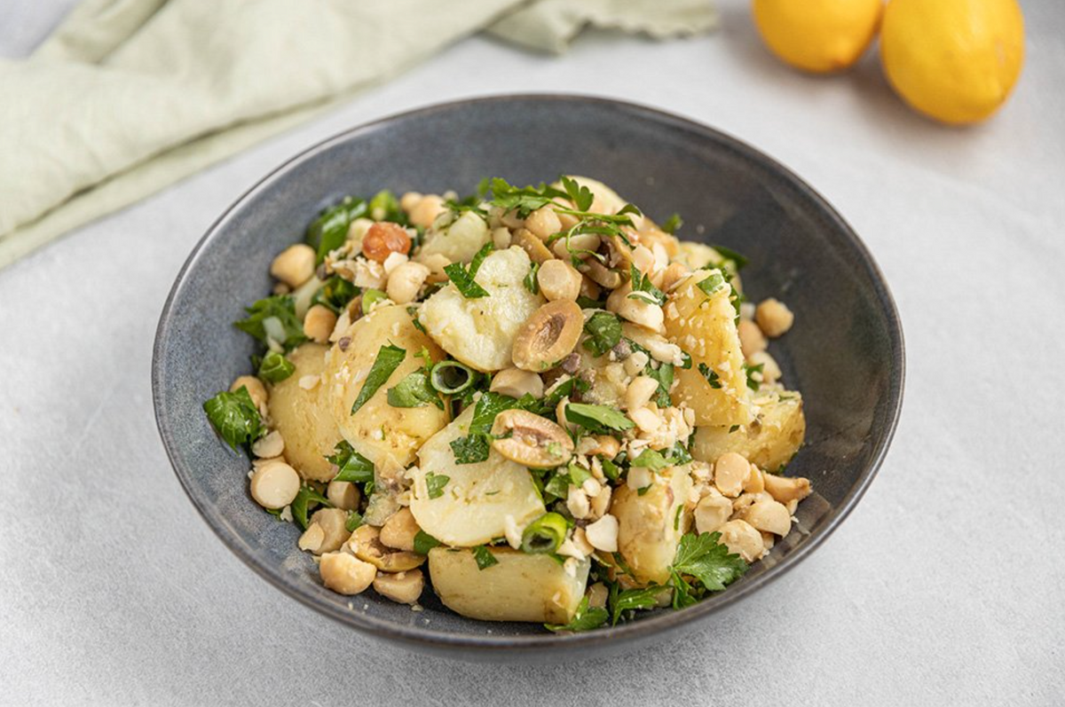 Warm potato and macadamia salad with fresh herbs and chickpeas in a dark bowl