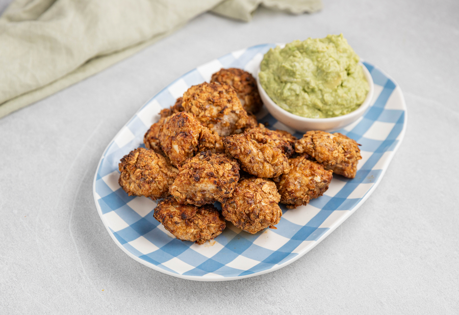 Chicken nuggets with nutty granola crumb and a side of guacamole on a blue checkered plate