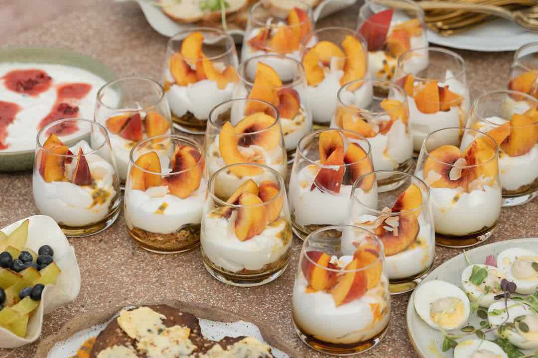 Mini glass cups filled with toasted muesli, creamy yogurt, and fresh peach slices.