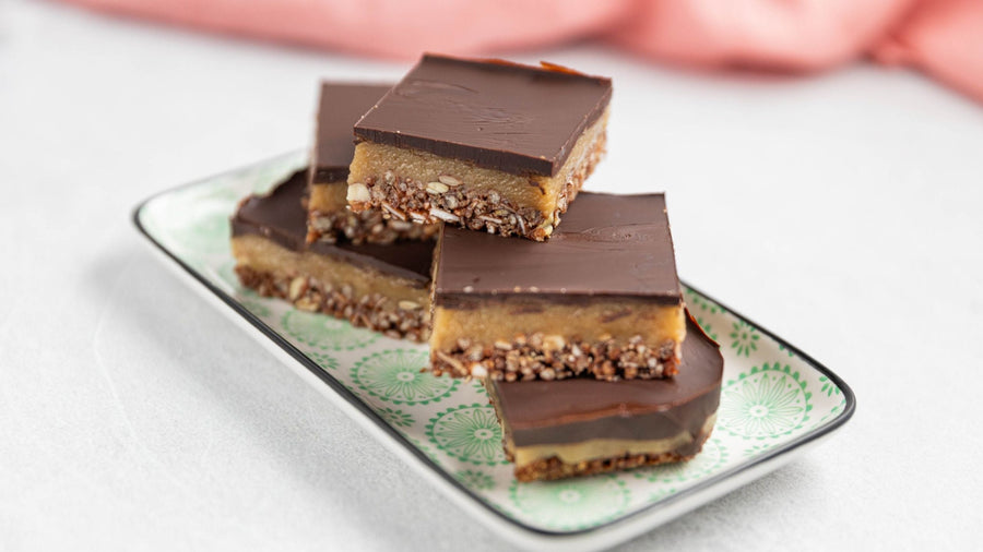 Stacked pieces of Tahini Caramel Granola Slice topped with dark chocolate on a decorative plate