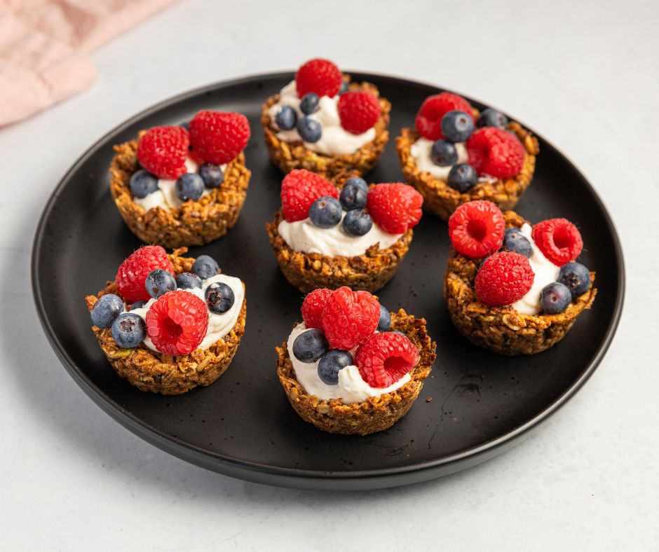 Mini vegan breakfast tarts made with granola, cream, raspberries, and blueberries on a black plate