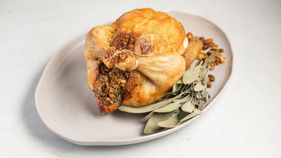 Golden roasted chicken with nut stuffing and fresh sage on a white platter