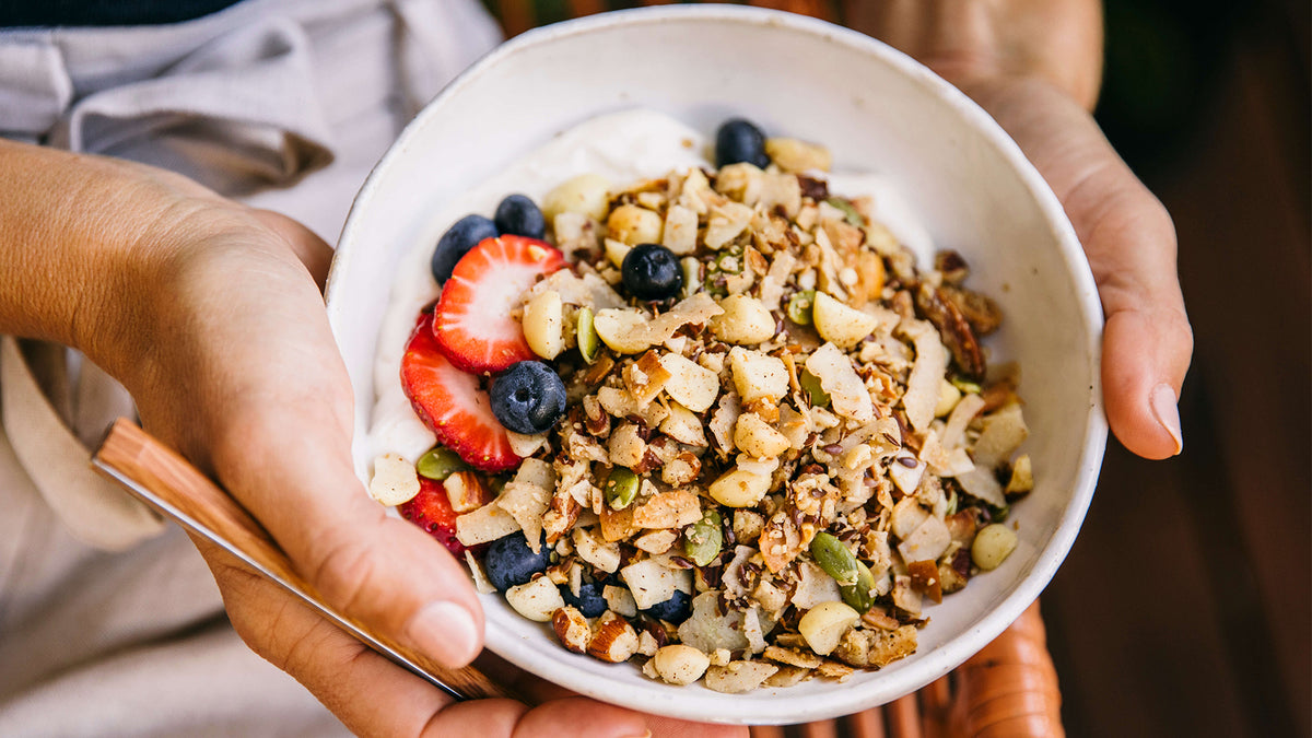 Bowl of Keto Premium Paleo Granola with strawberries, blueberries and yoghurt being held by woman